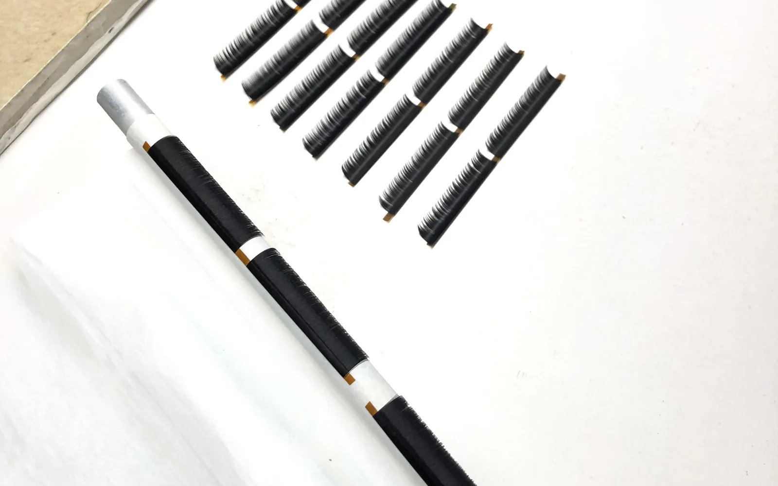 A curl rod with black lash fiber beside strips already cut to row length