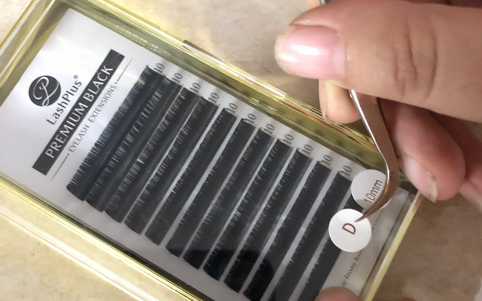 Tweezers setting a finished row into a gold-rimmed Premium Black tray case, a D curl label ready to go on