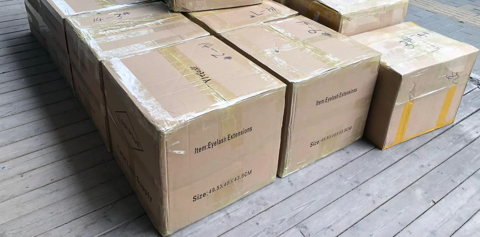 LashPlus export cartons of lash supplies wrapped and stacked on the loading deck, each marked Item: Eyelash Extensions with its carton size